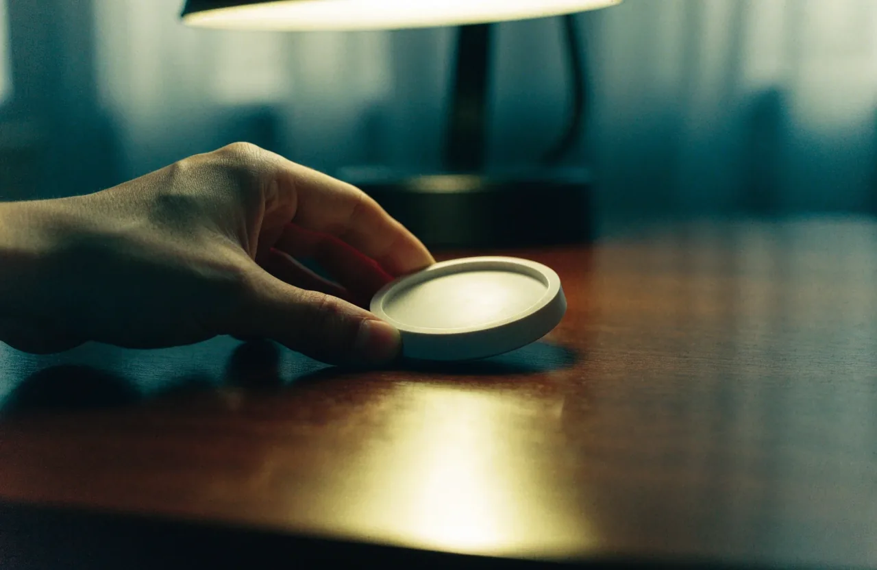 A hand holding a plain unbranded supplement plate under a warm lamp